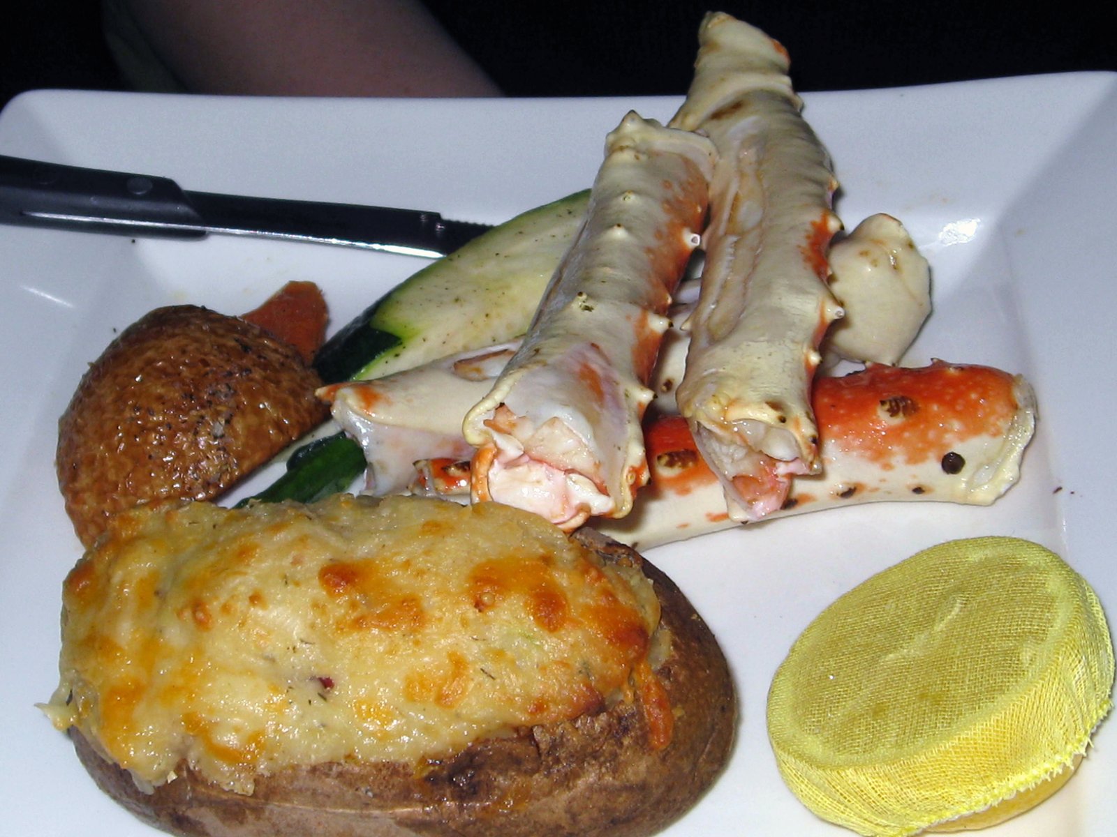 A plate piled with crab legs and a stuffed baked potato, buffet-style
